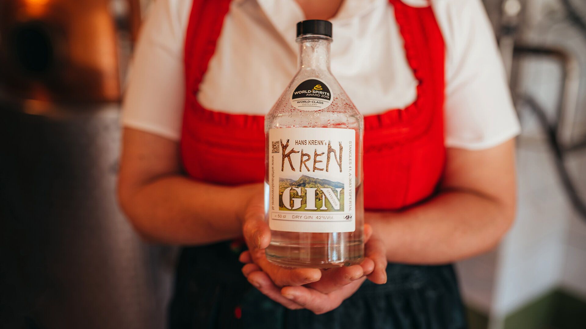 In der Wirtshausbrennerei Krenn entfaltet sich der unverwechselbare Charakter des Gins, der mit viel Liebe und handwerklichem Geschick hergestellt wird. Die klare Flasche, die von der Wirtin Martina Krenn gehalten wird, spiegelt die Tradition und die Leidenschaft für die Destillation wider. Hier im Waldviertel wird jeder Schluck zu einem Erlebnis, das die Sinne verführt.