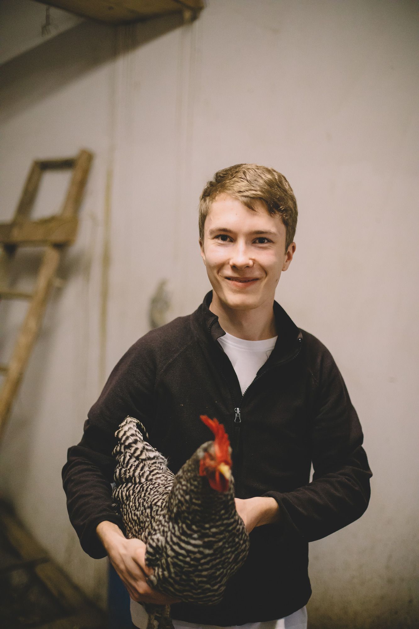 Ein junger Mann hält ein Huhn in einem Innenraum.