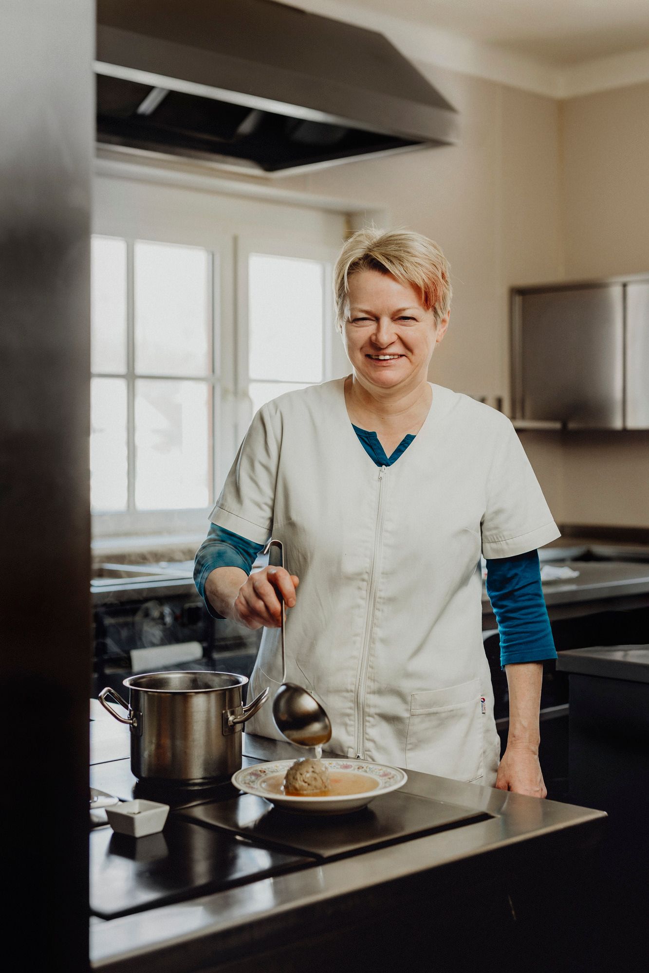 Eine Köchin in weißer Uniform serviert Suppe in einer Küche.