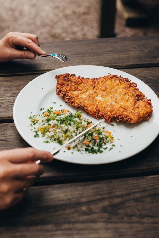 A plate with a breaded schnitzel and rice vegetables on a wooden table.