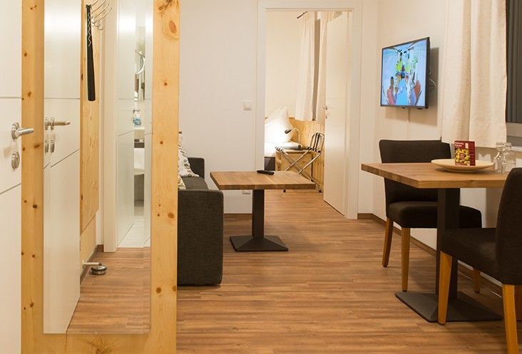 Modern eingerichtetes Zimmer mit Holzboden, Sofa, Esstisch und Fernseher an der Wand.