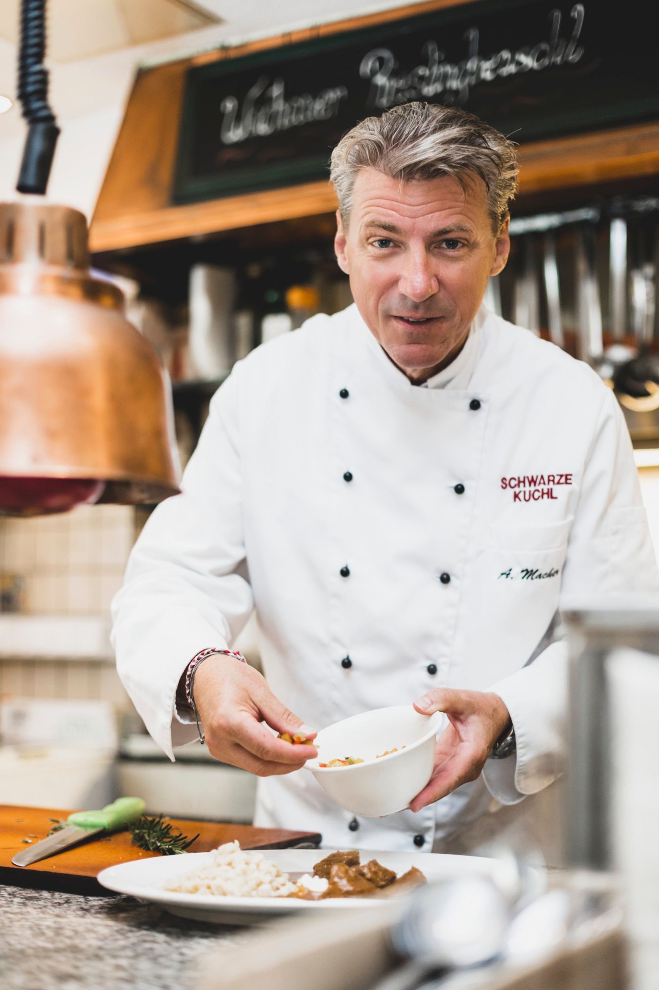 Koch in weißer Uniform bereitet ein Gericht in einer Küche zu.