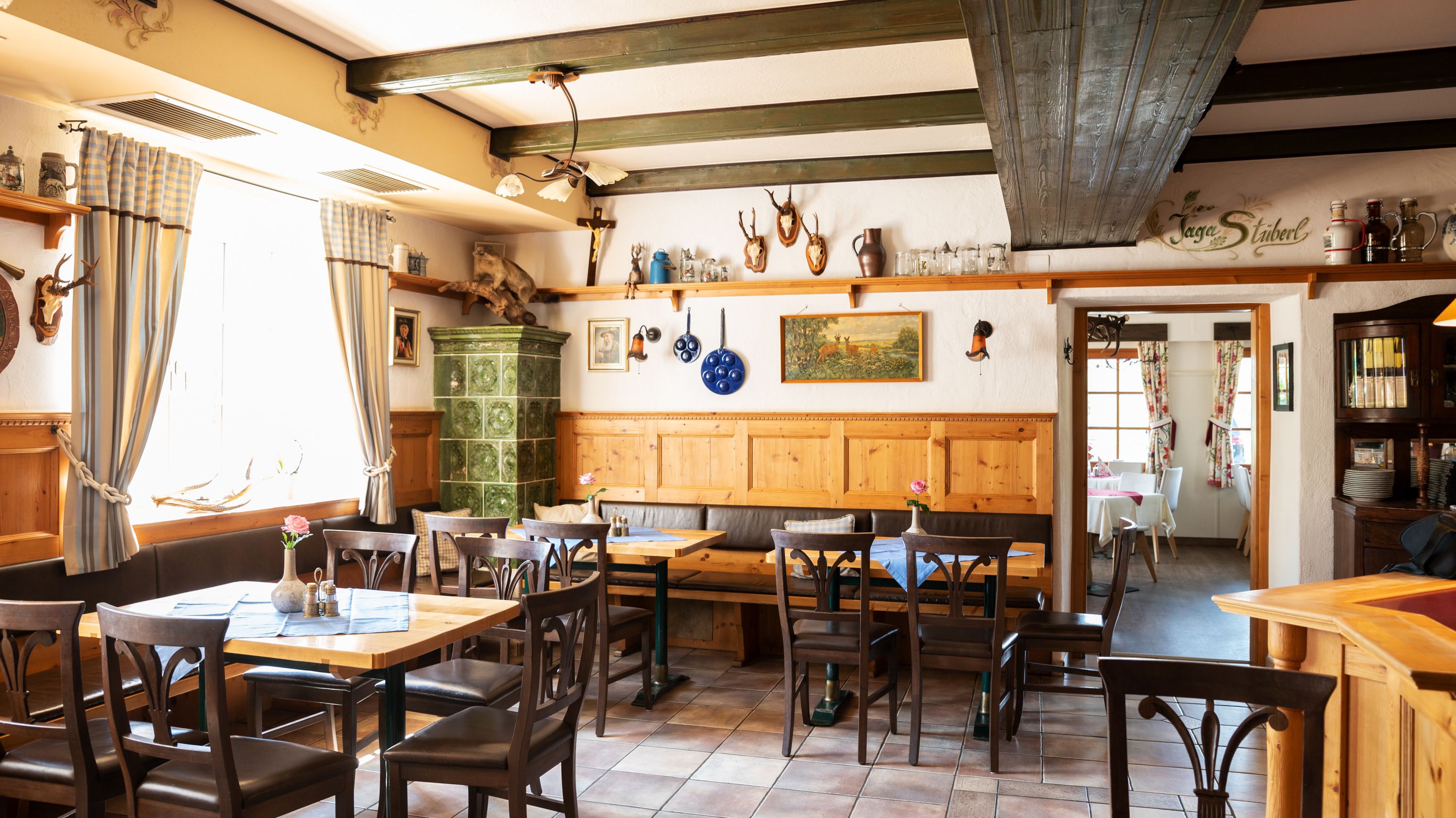 Gemütliche Stube mit Holzmöbeln, Kachelofen und Jagdtrophäen an den Wänden.