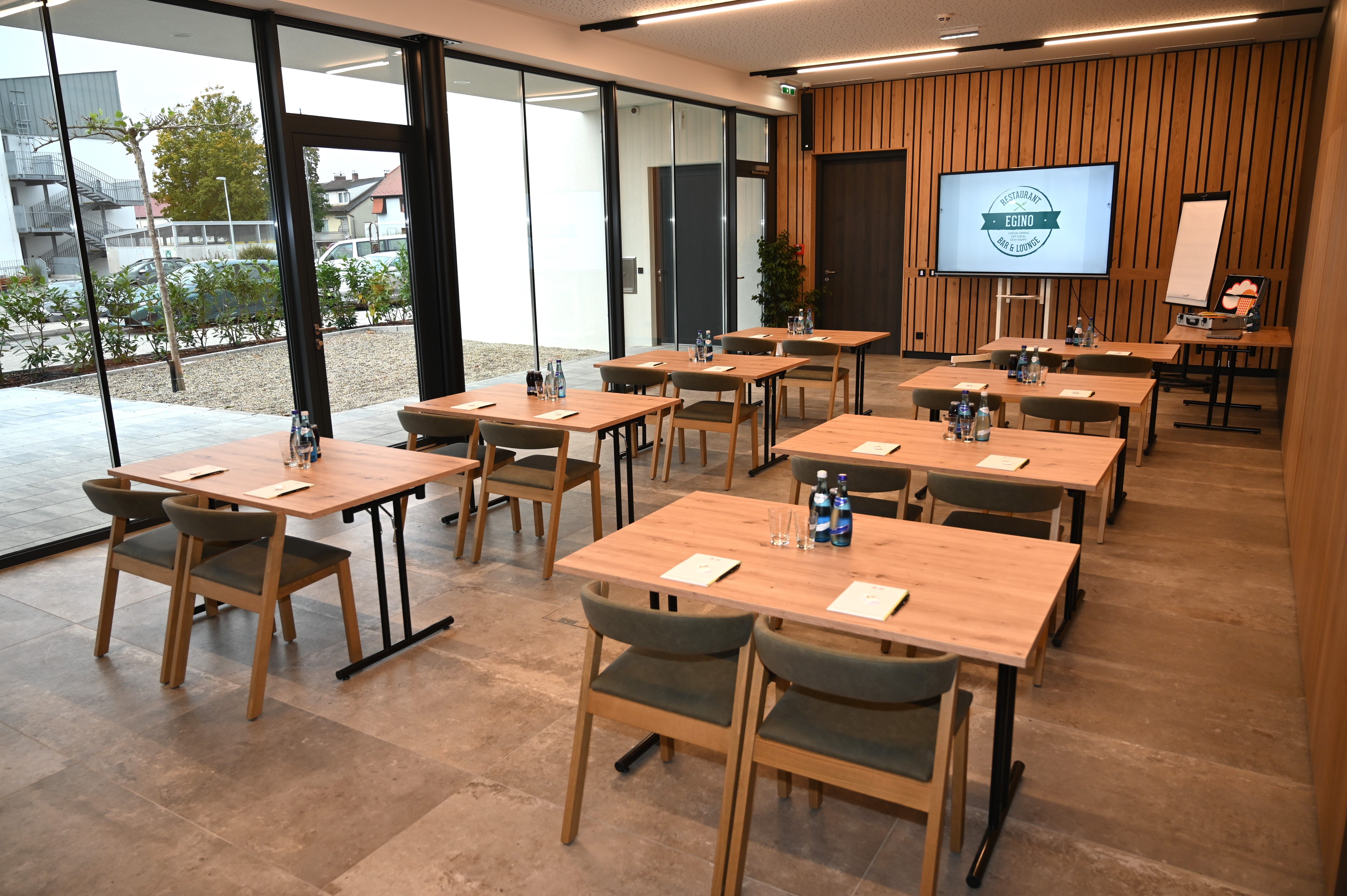 Moderner Seminarraum mit Holztischen, Stühlen und Präsentationstechnik.