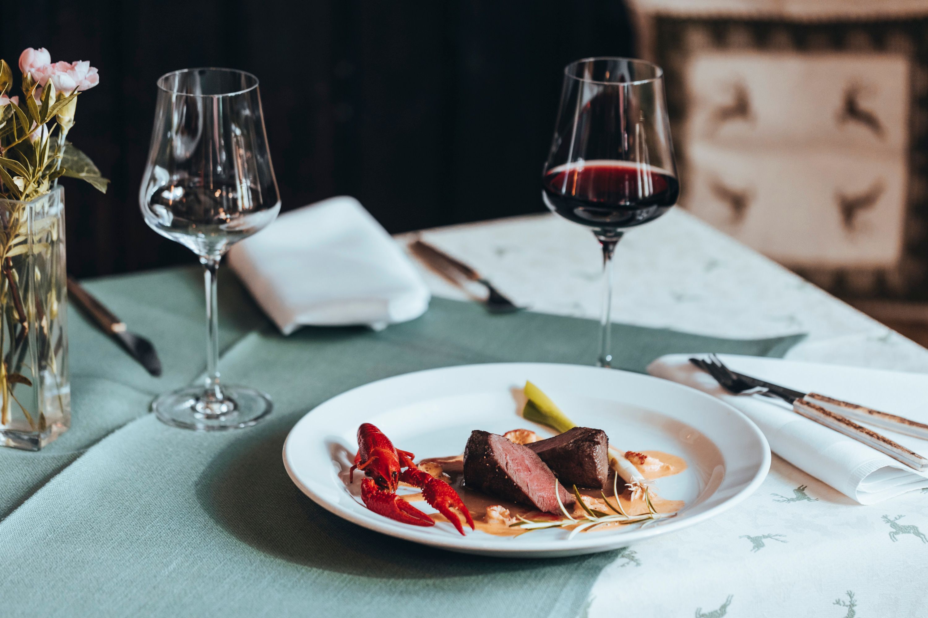 Elegantes Abendessen mit Fleisch, Flusskrebs und Rotwein auf gedecktem Tisch.