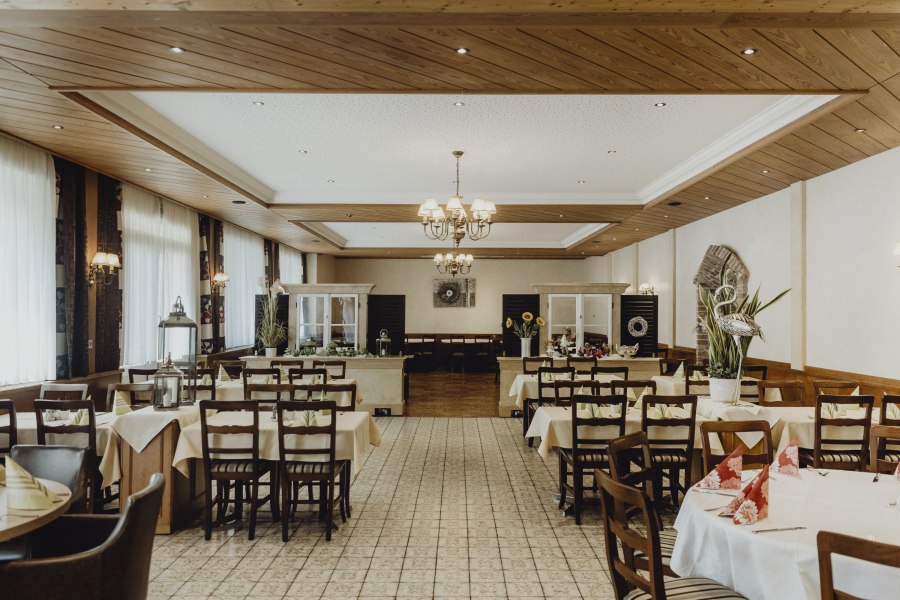 Innenansicht eines traditionellen Wirtshauses mit gedeckten Tischen und Holzdecke.