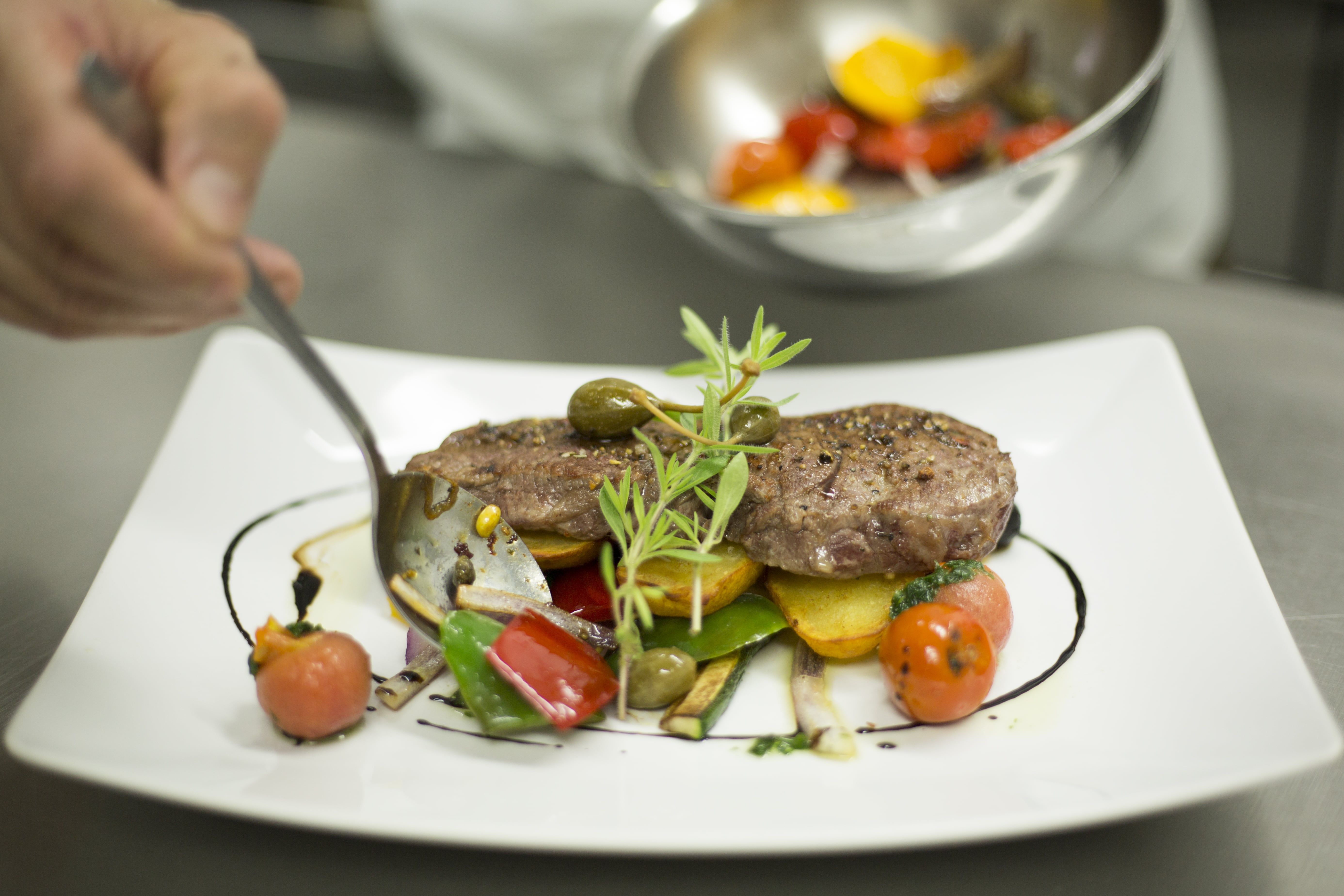 Ein Teller mit kunstvoll angerichtetem Fleisch, Gemüse und Kräutern.