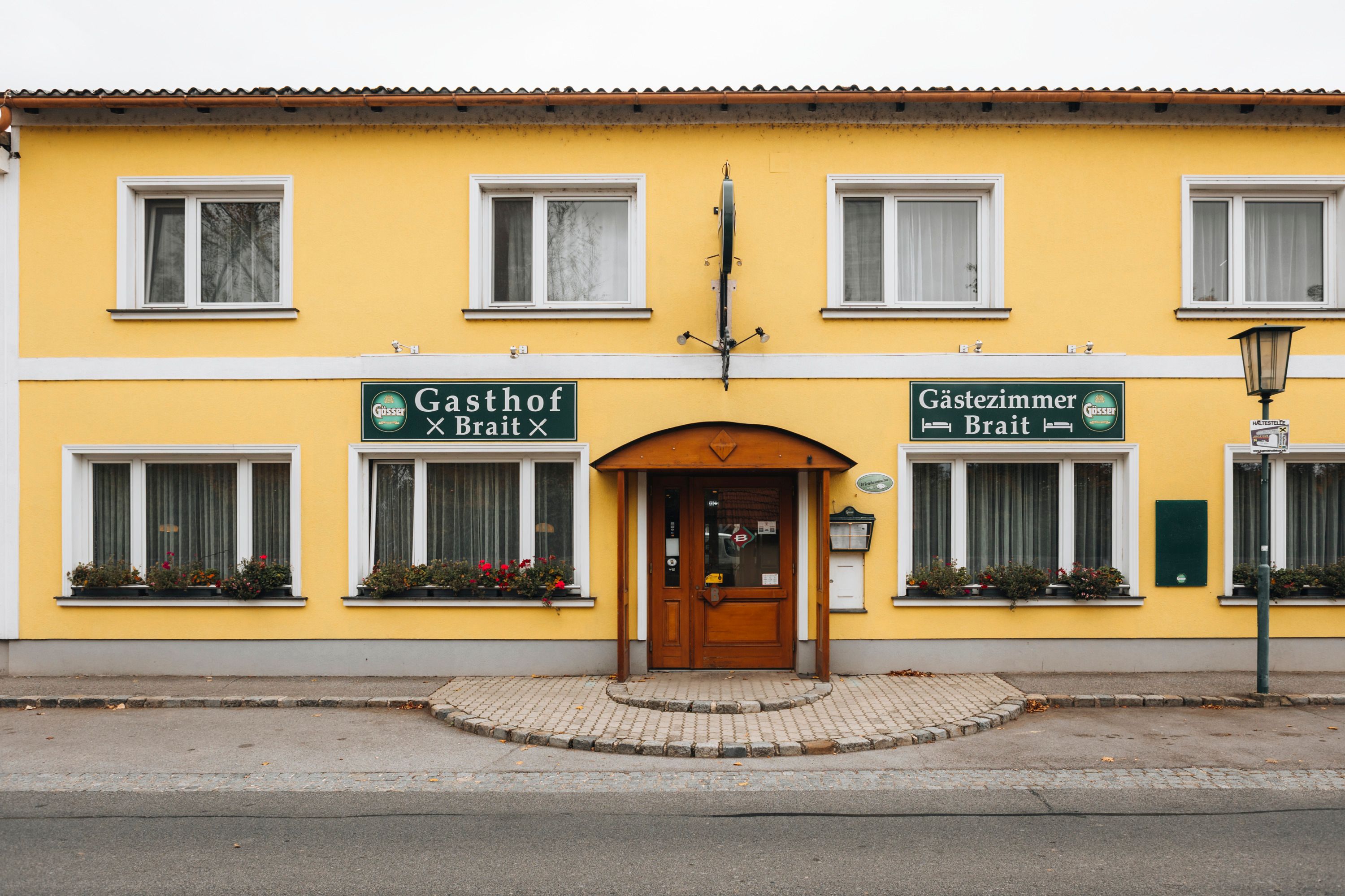 Gelbes Gebäude mit Schildern 'Gasthof Brait' und 'Gästezimmer Brait'.