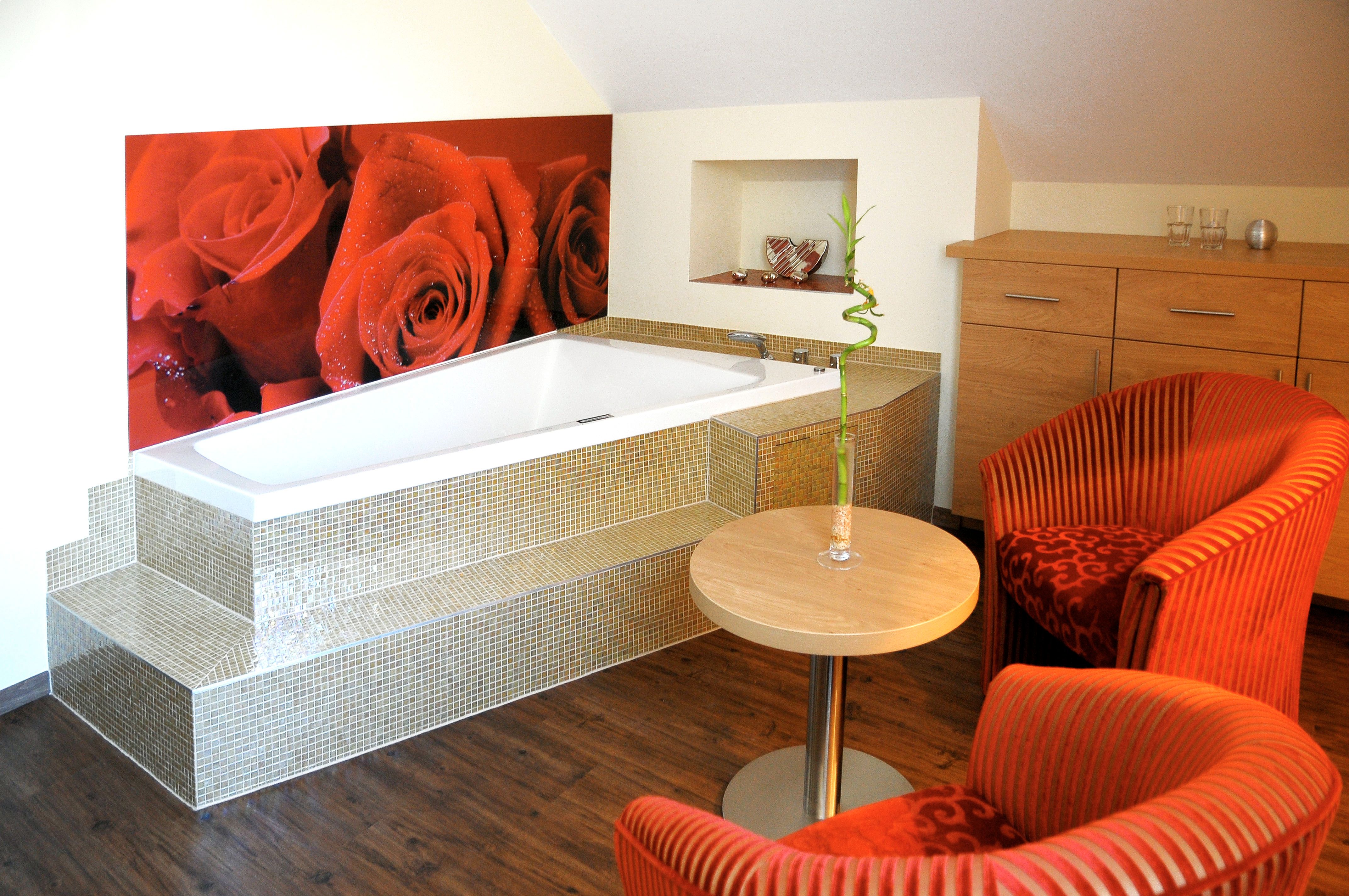 Gemütliches Zimmer mit Badewanne, roten Sesseln und Rosenbild an der Wand.