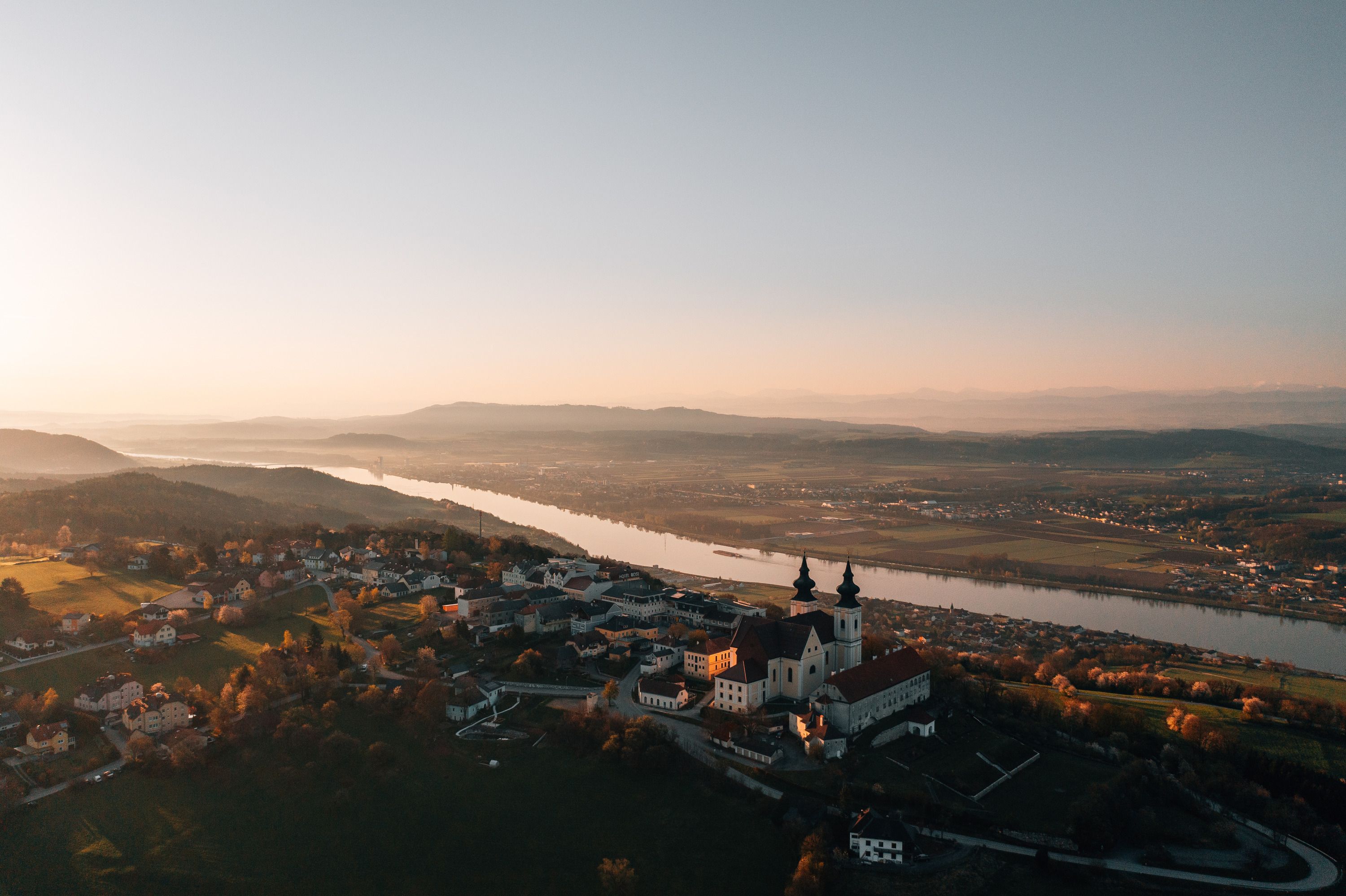 Luftaufnahme einer Kirche bei Sonnenuntergang, umgeben von Fluss und Landschaft.