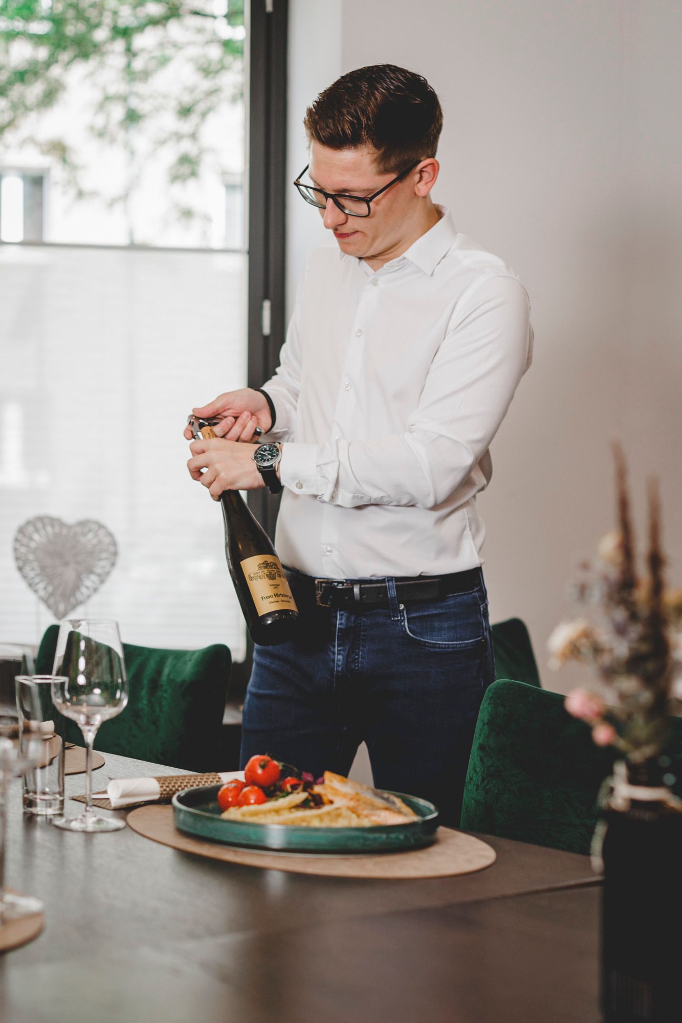Ein Mann öffnet eine Weinflasche an einem gedeckten Tisch mit Essen.