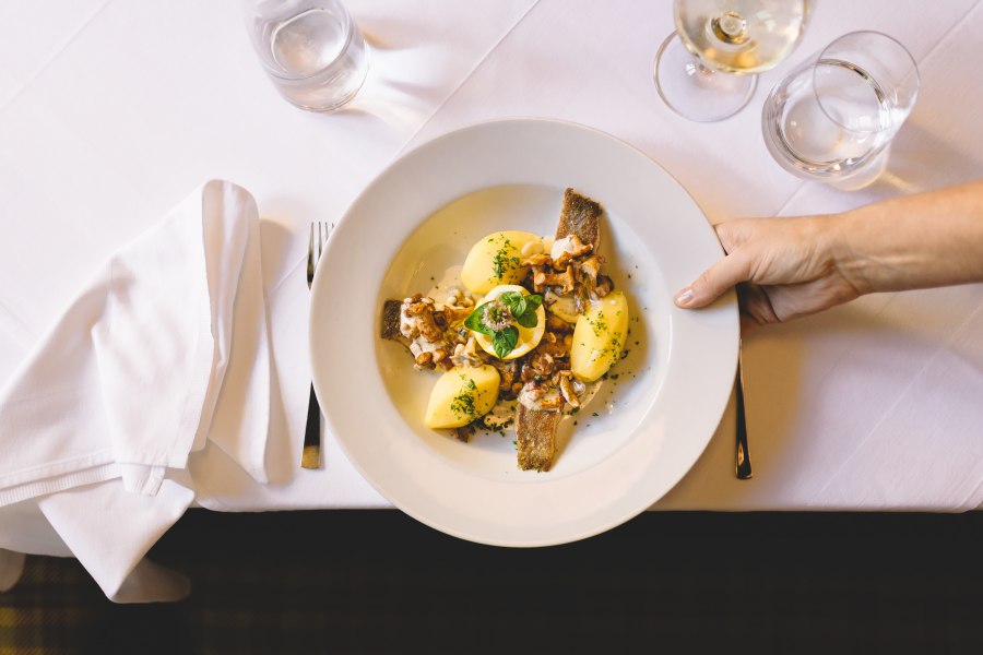 Ein Teller mit Karpfen, Kartoffeln und Pilzen auf einem wei&szlig; gedeckten Tisch.