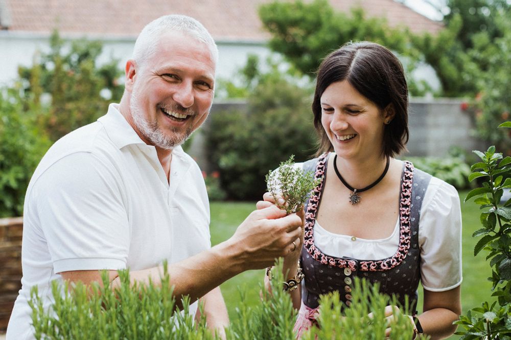 Ein Mann und eine Frau stehen lächelnd in einem Garten und betrachten Kräuter.