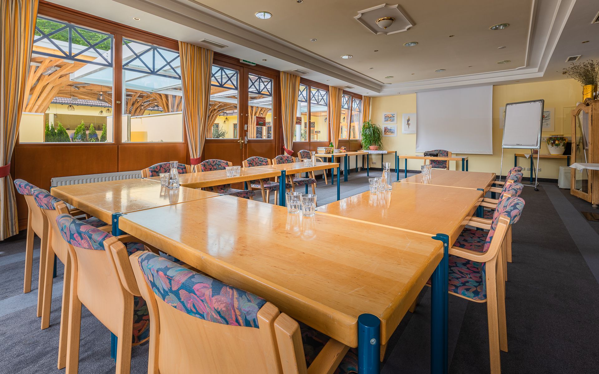 Ein heller Seminarraum mit großen Fenstern, Tischen in U-Form, Stühlen und einem Flipchart.