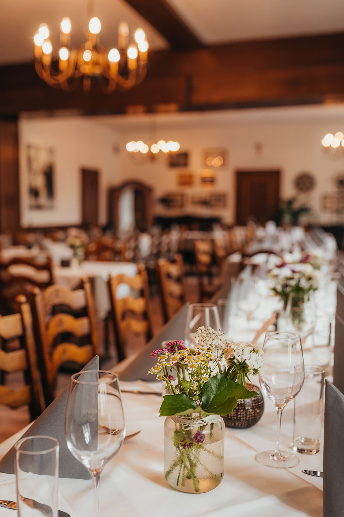Ein eleganter Speisesaal mit gedeckten Tischen, Blumenarrangements und einem Kronleuchter an der Decke.