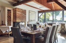 Elegantes Restaurant mit Holzbalken, Kamin und gedeckten Tischen.
