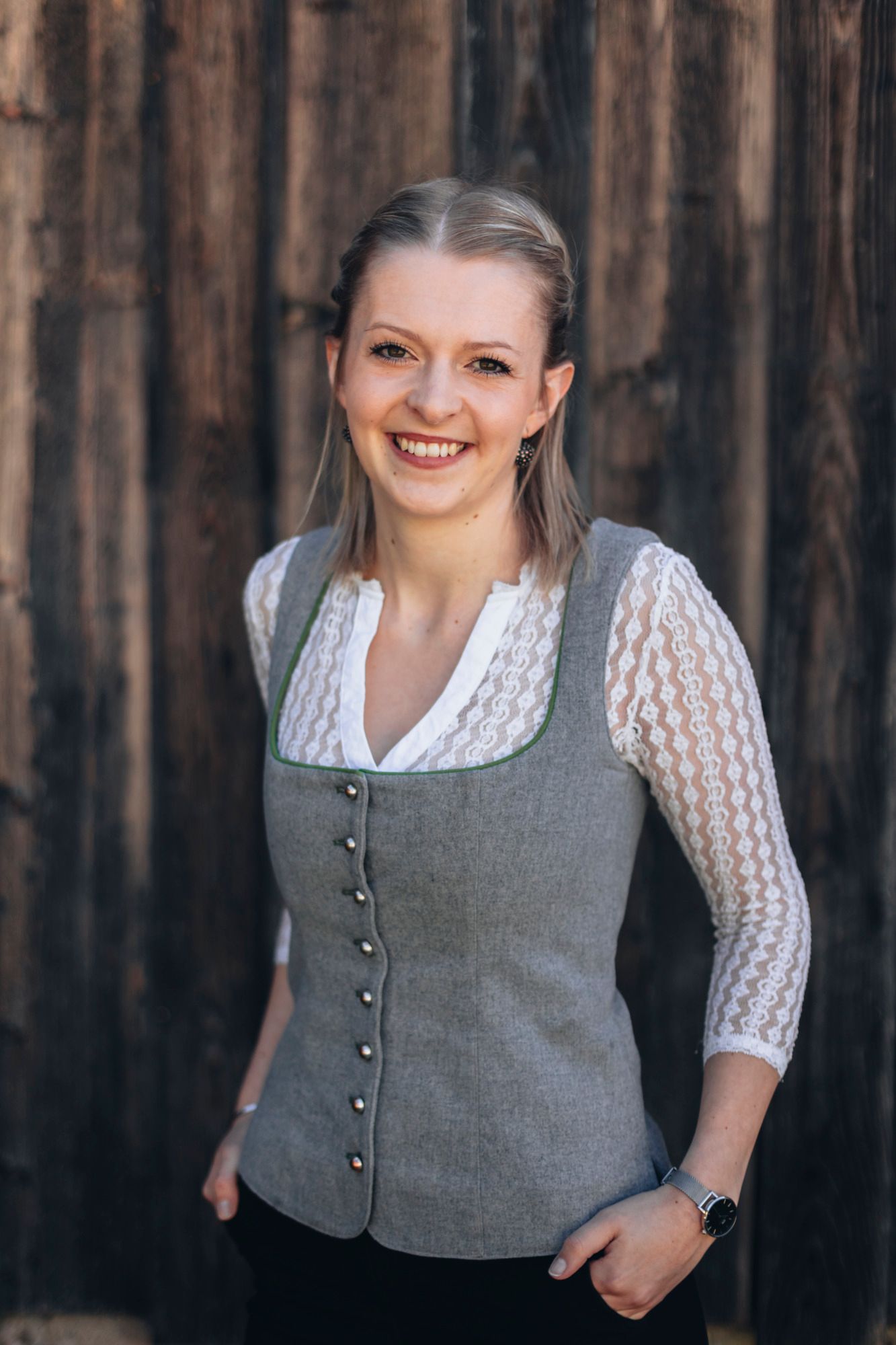 Frau in traditioneller Kleidung vor Holzwand.