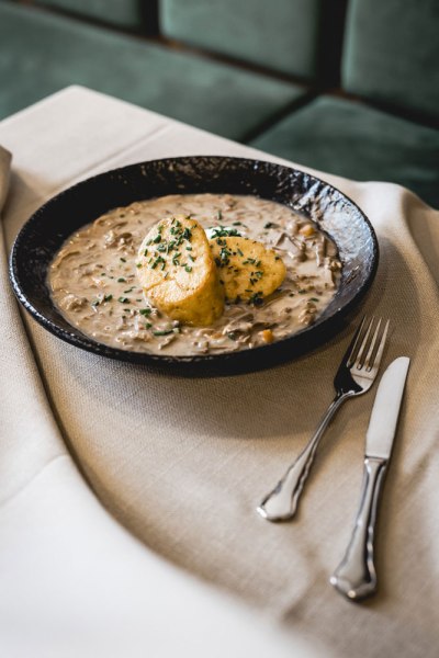 Ein Teller mit Beuschl und zwei Semmelkn&ouml;deln, garniert mit Kr&auml;utern, auf einem Tisch mit Besteck.