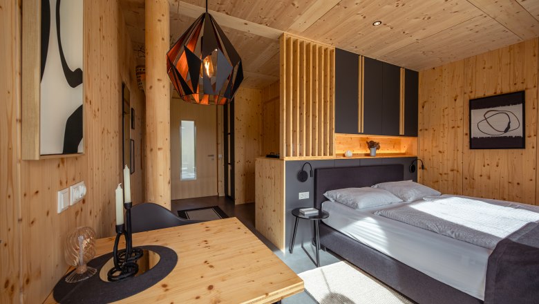 Modernes Schlafzimmer mit Holzwänden, einem Bett, einem Tisch und einer geometrischen Hängelampe.