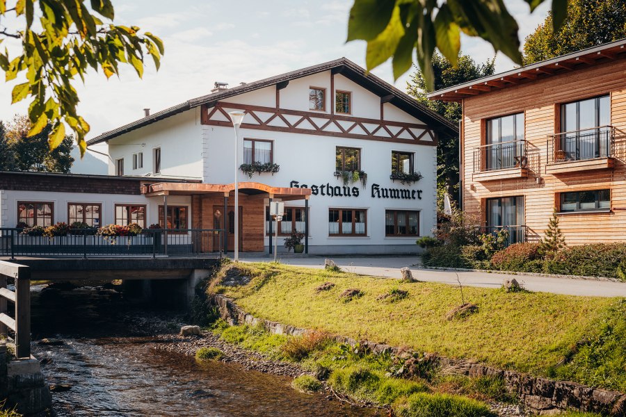 Ein traditionelles Gasthaus mit wei&szlig;er Fassade und Holzverzierungen neben einem Bach.