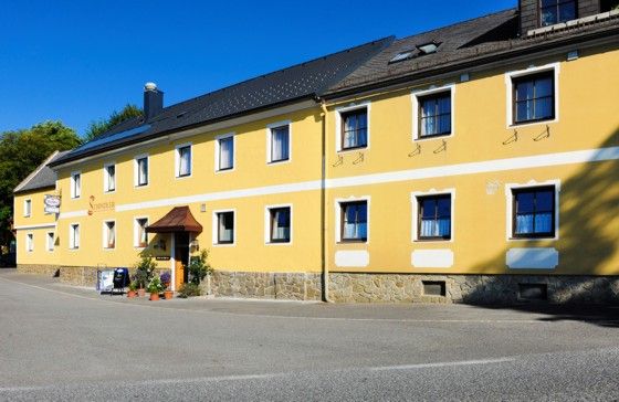 Gelbes Gebäude mit mehreren Fenstern und einem Eingang, beschriftet als Gasthof Schindler.