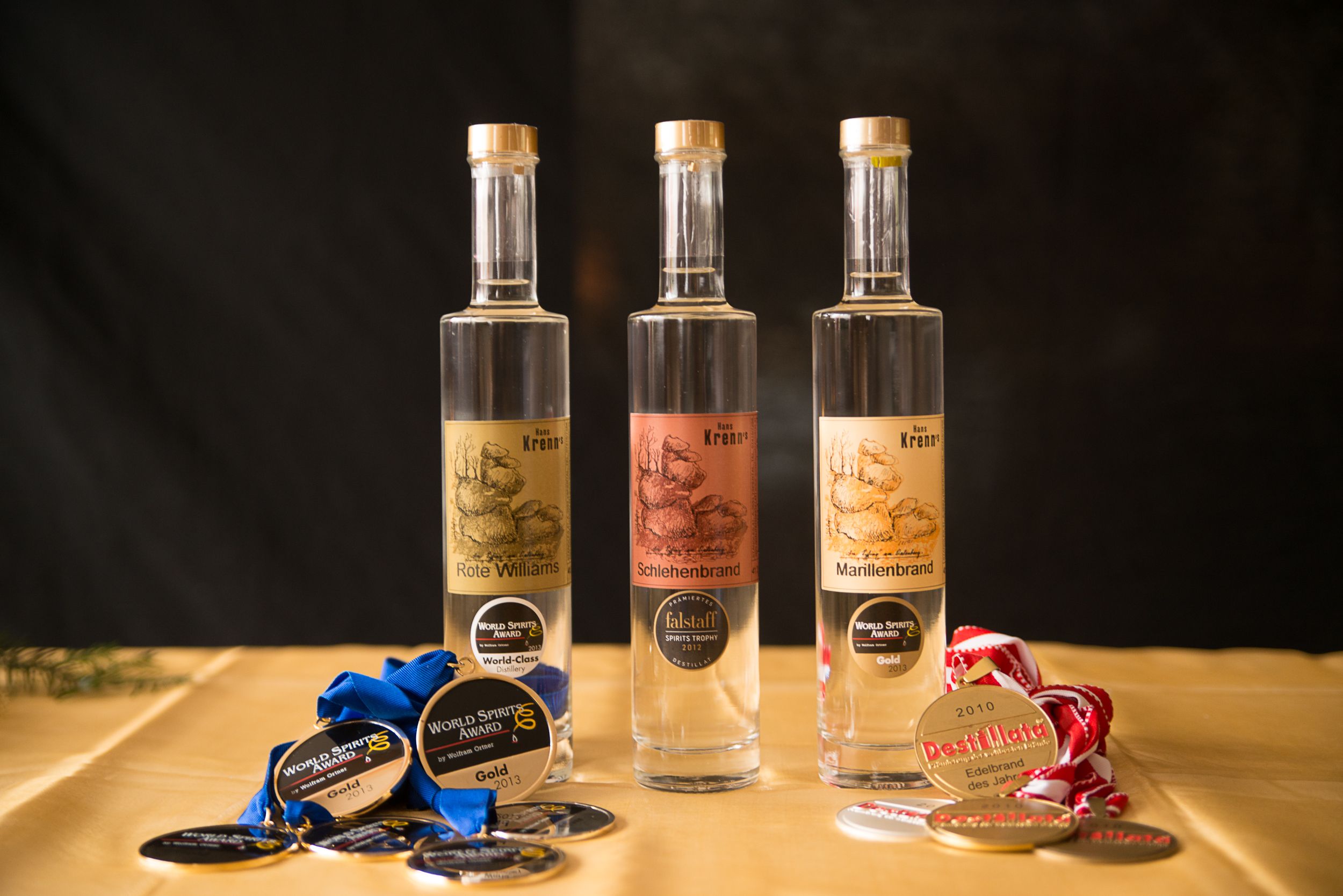Drei Flaschen Edelbrand mit Medaillen auf einem Tisch.