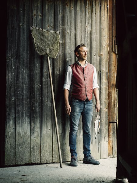 Ein Mann in traditioneller Kleidung steht neben einem Fischernetz und h&auml;lt einen Fisch in der Hand.
