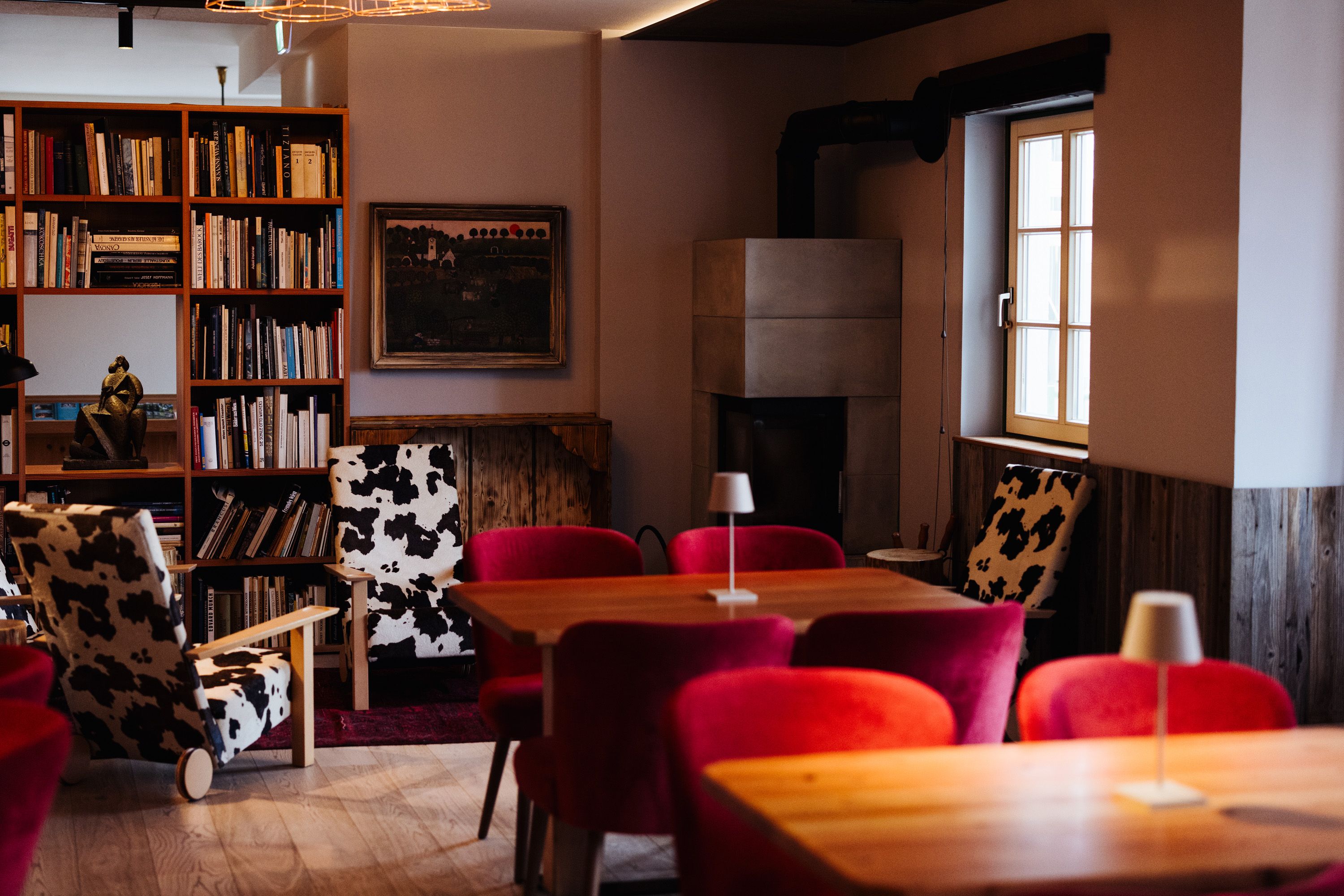 Gemütlicher Raum mit Kamin, Bücherregal, roten Sesseln und Kuhfellstühlen.