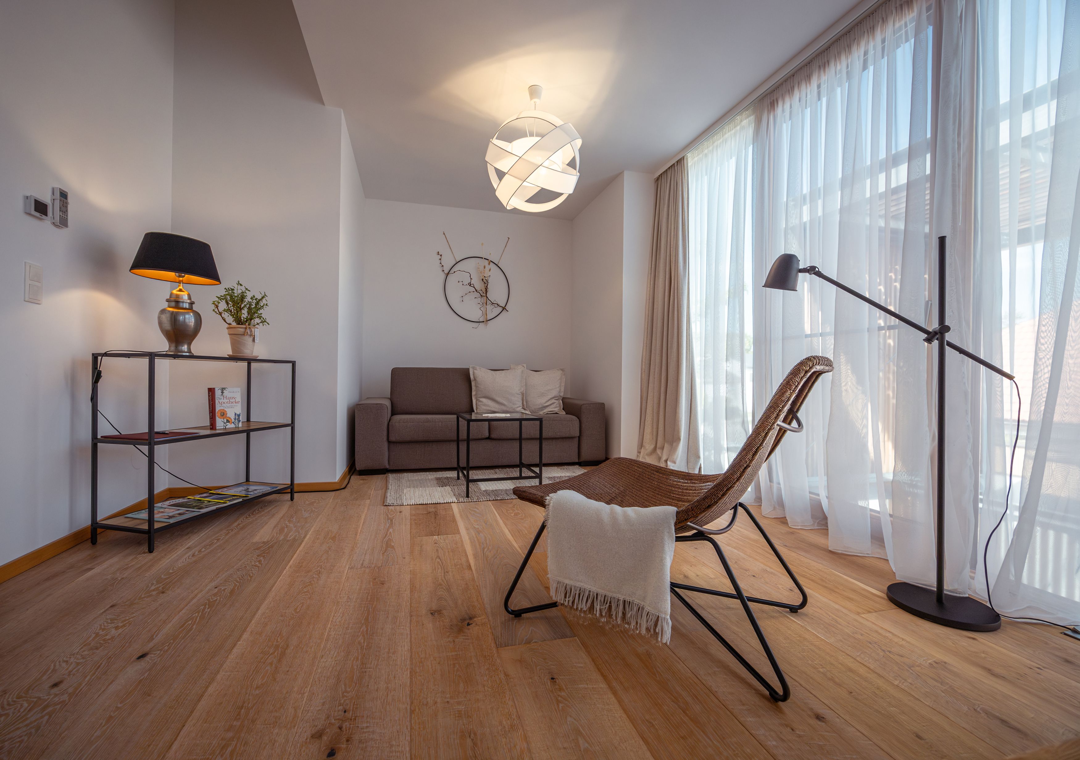 Modern furnished living room with sofa, armchair, floor lamp and large window with curtains.