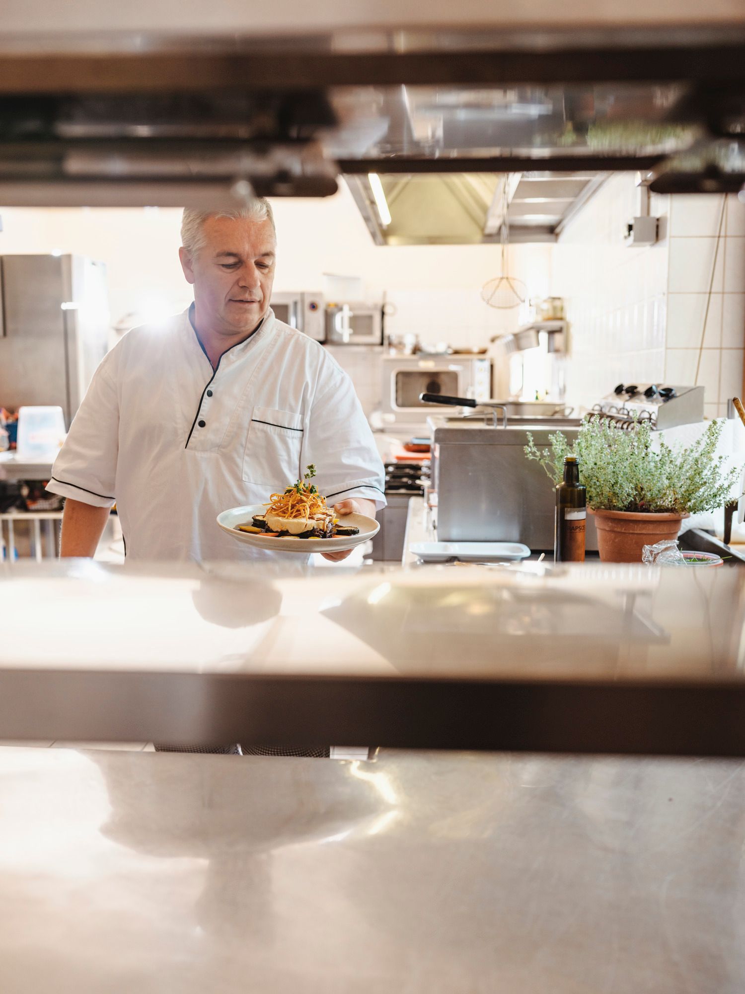 Ein Koch in einer Restaurantküche hält einen Teller mit Essen in der Hand.