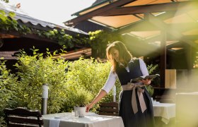 Eine Frau in traditioneller Kleidung richtet einen Tisch im Garten eines Landgasthauses her.