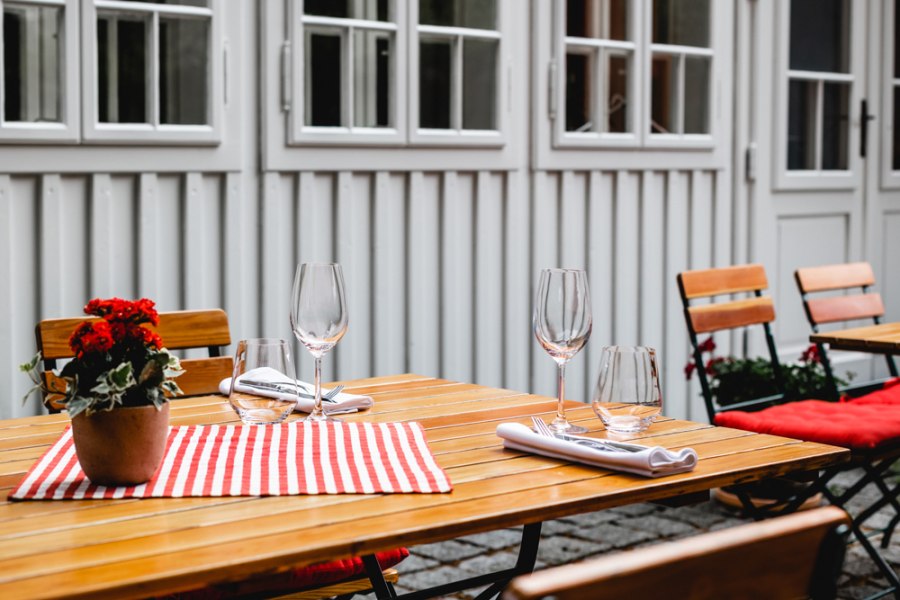 Gedeckter Holztisch im Freien mit Blumen und Gl&auml;sern.