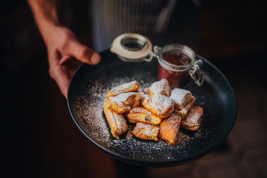 Ein Teller mit Kaiserschmarren, bestäubt mit Puderzucker, und einem Glas Zwetschkenröster.