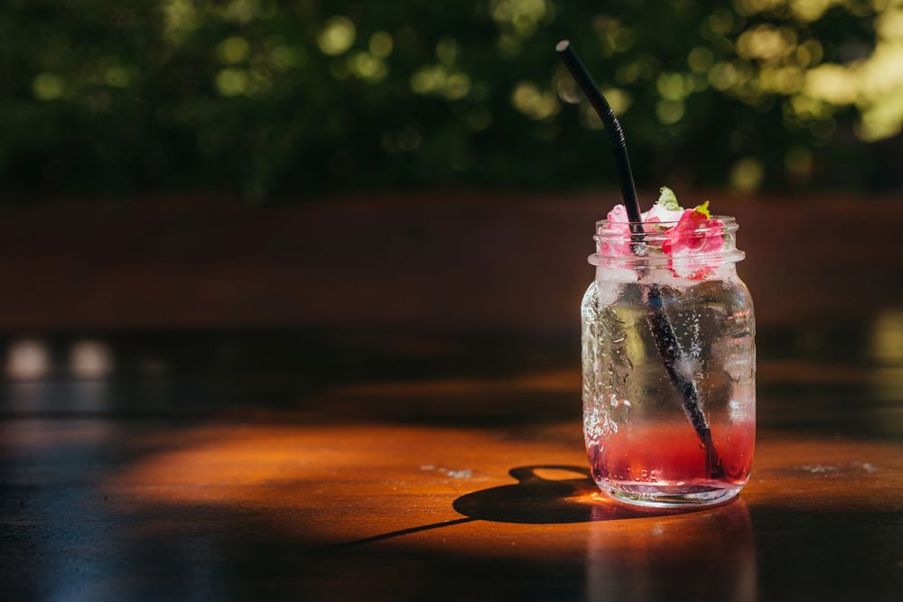 Ein Glas mit rotem Getränk und schwarzem Strohhalm auf einem Holztisch.