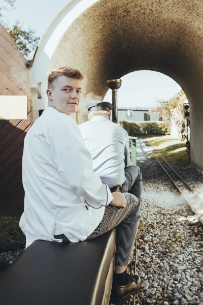 Zwei Personen sitzen auf einer dampfbetriebenen Minibahn, die durch einen Tunnel fährt.