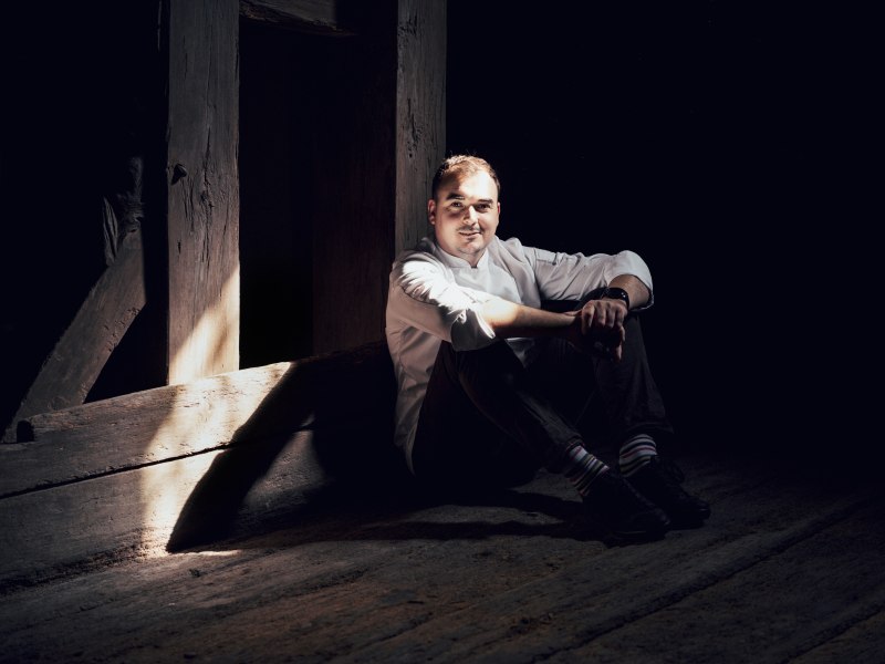 Mann in weißem Hemd sitzt im Schatten auf Holzboden.