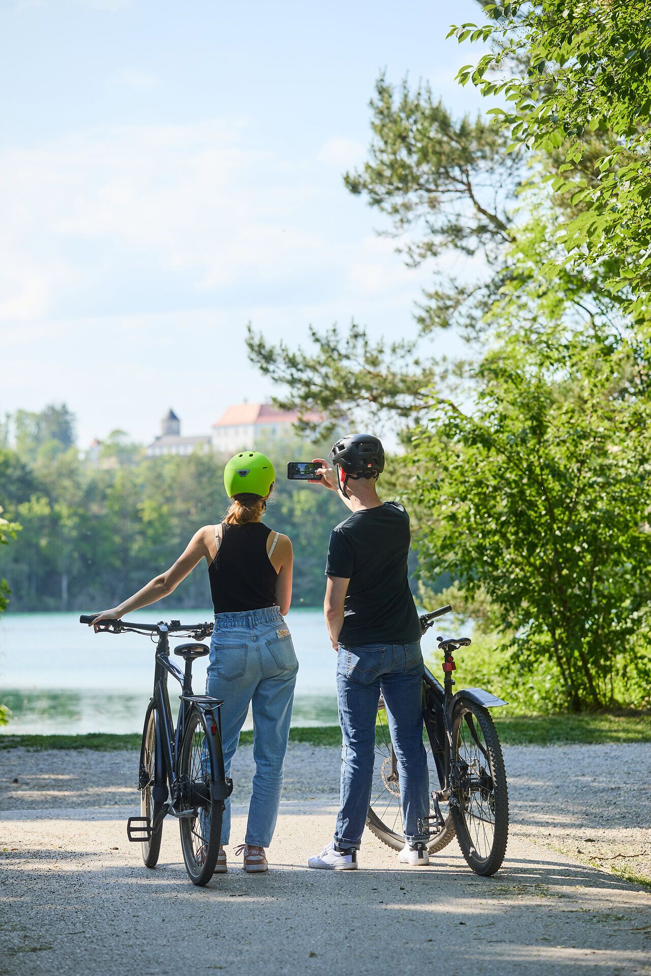 Zwei Radfahrer genießen die frische Luft und die malerische Aussicht auf den glitzernden See, umgeben von üppigem Grün. Die sanften Hügel und die ruhige Atmosphäre laden dazu ein, die Schönheit der Natur zu erkunden und unvergessliche Momente zu erleben.