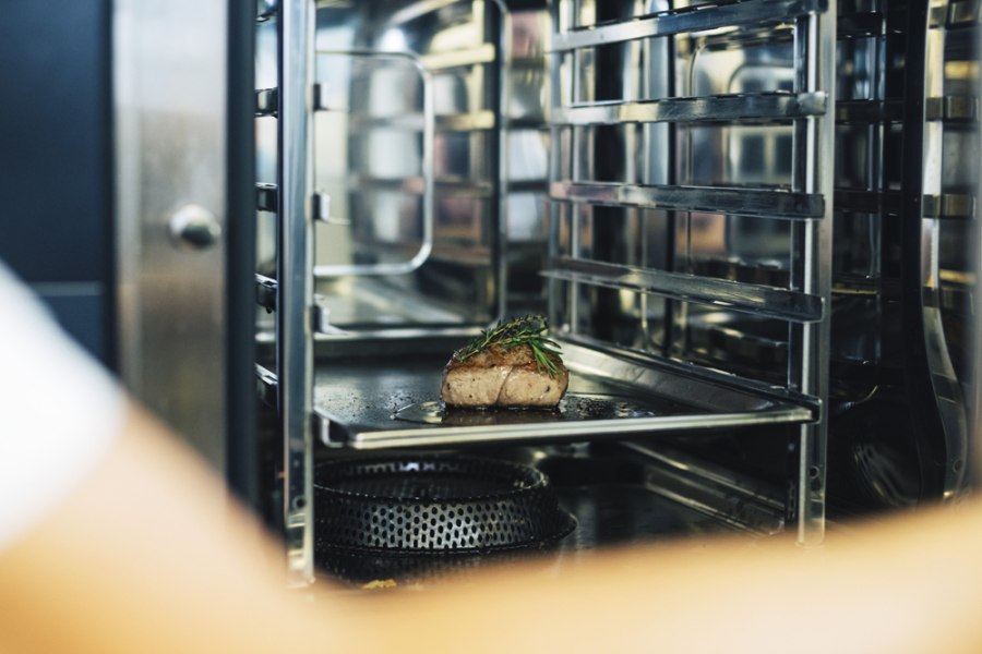 Ein St&uuml;ck Fleisch mit Kr&auml;utern in einem professionellen Ofen.