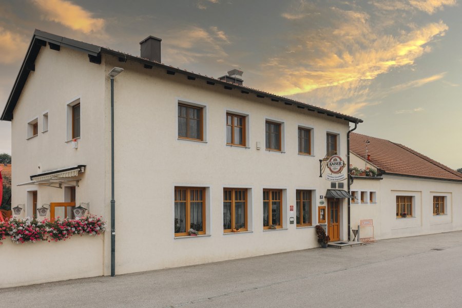 Gasthaus mit Blumenschmuck und Kaiser-Bierschild bei Sonnenuntergang.