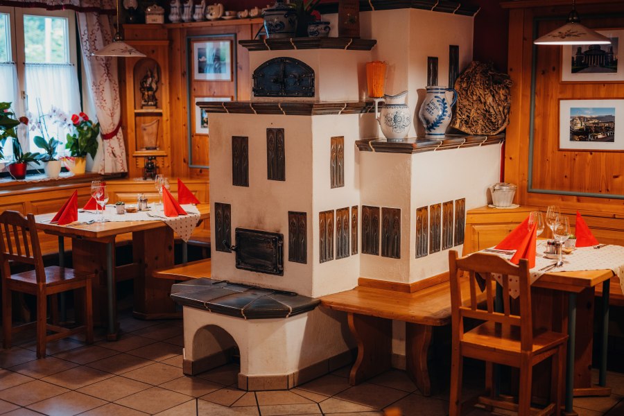 Gem&uuml;tliche Stube mit Kachelofen, Holzm&ouml;beln und gedeckten Tischen.