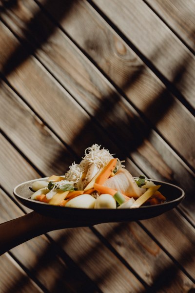 Ein Teller mit Krenfleisch, Gem&uuml;se und geriebenem Kren vor einer Holzwand.