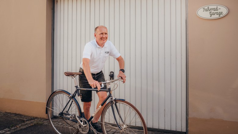 Mann in weißem Polohemd fährt Fahrrad vor Garagentor.