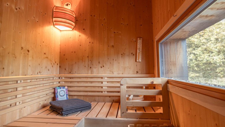 Innenansicht einer Holzsauna mit Bänken, Handtuch und Fenster.