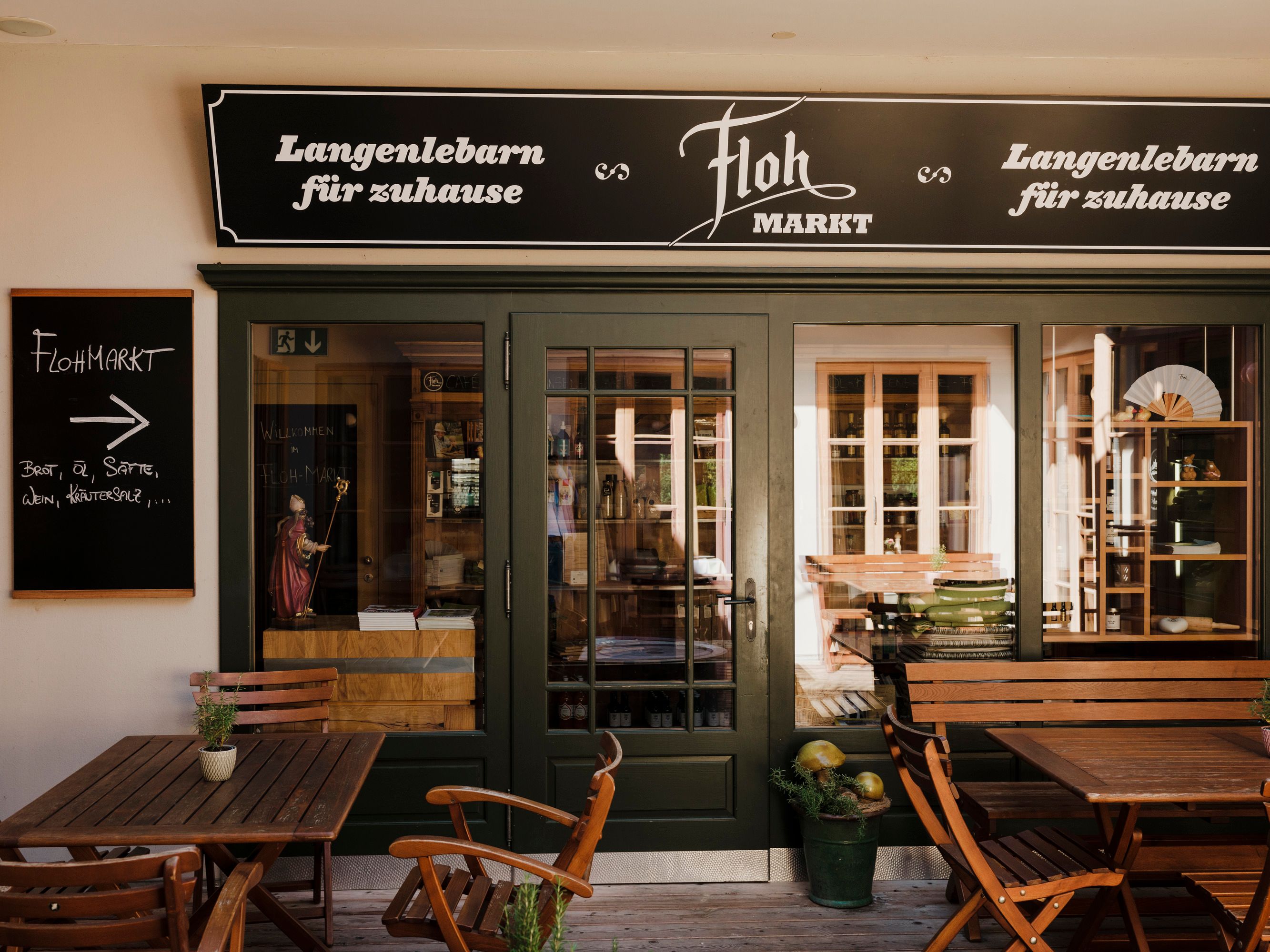 Eingang zu einem regionalen Laden mit Schildern, Holztischen und Stühlen.