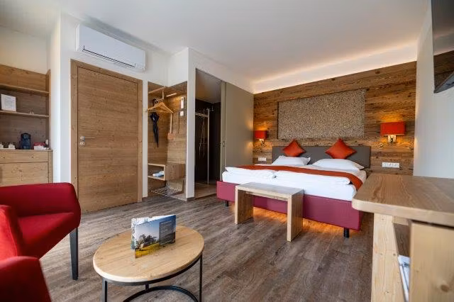 Modernes Gästezimmer mit Doppelbett, Holzmöbeln und roten Akzenten.
