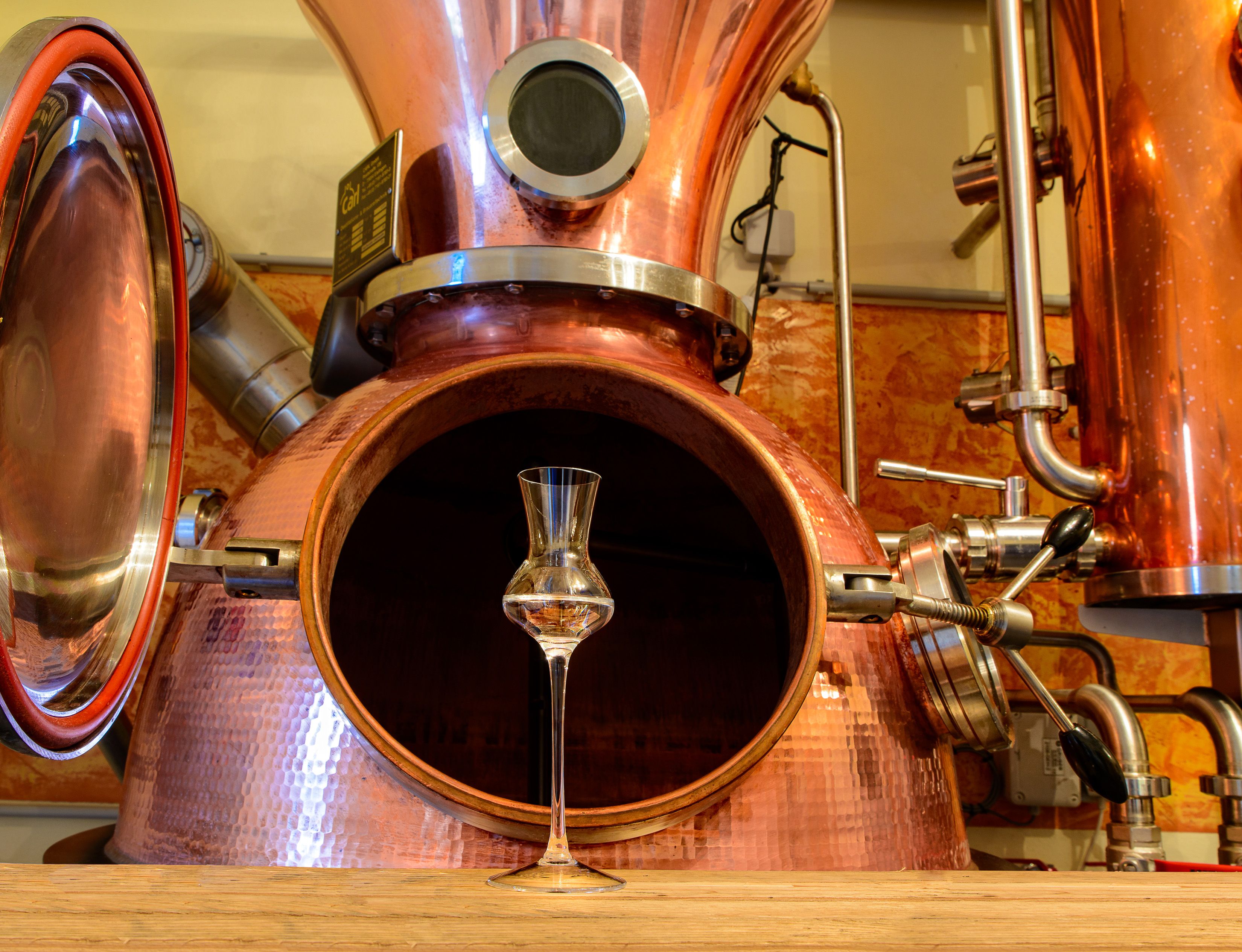 Kupferne Destillationsanlage mit einem Schnapsglas im Vordergrund.