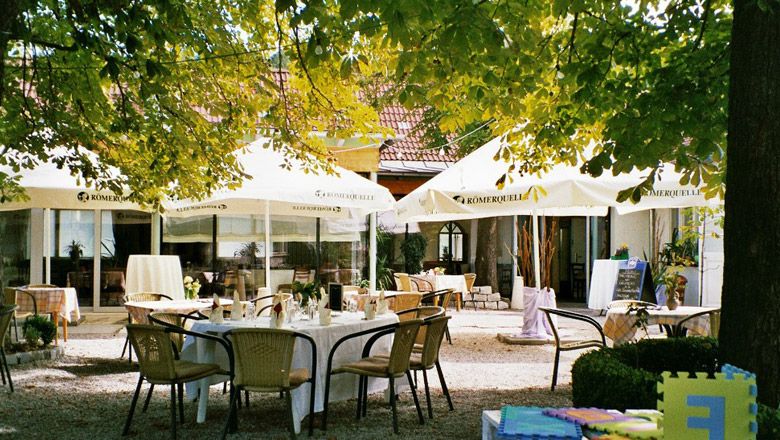 Ein gemütlicher Gastgarten mit Tischen und Stühlen unter großen Sonnenschirmen.
