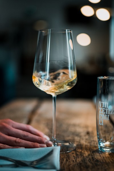 Ein Weinglas mit Wei&szlig;wein auf einem Holztisch, daneben ein Glas mit der Aufschrift 'Vinzenz Pauli'.