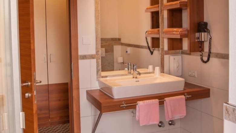 Modernes Badezimmer mit Waschbecken, Spiegel, Handtüchern und Föhn.