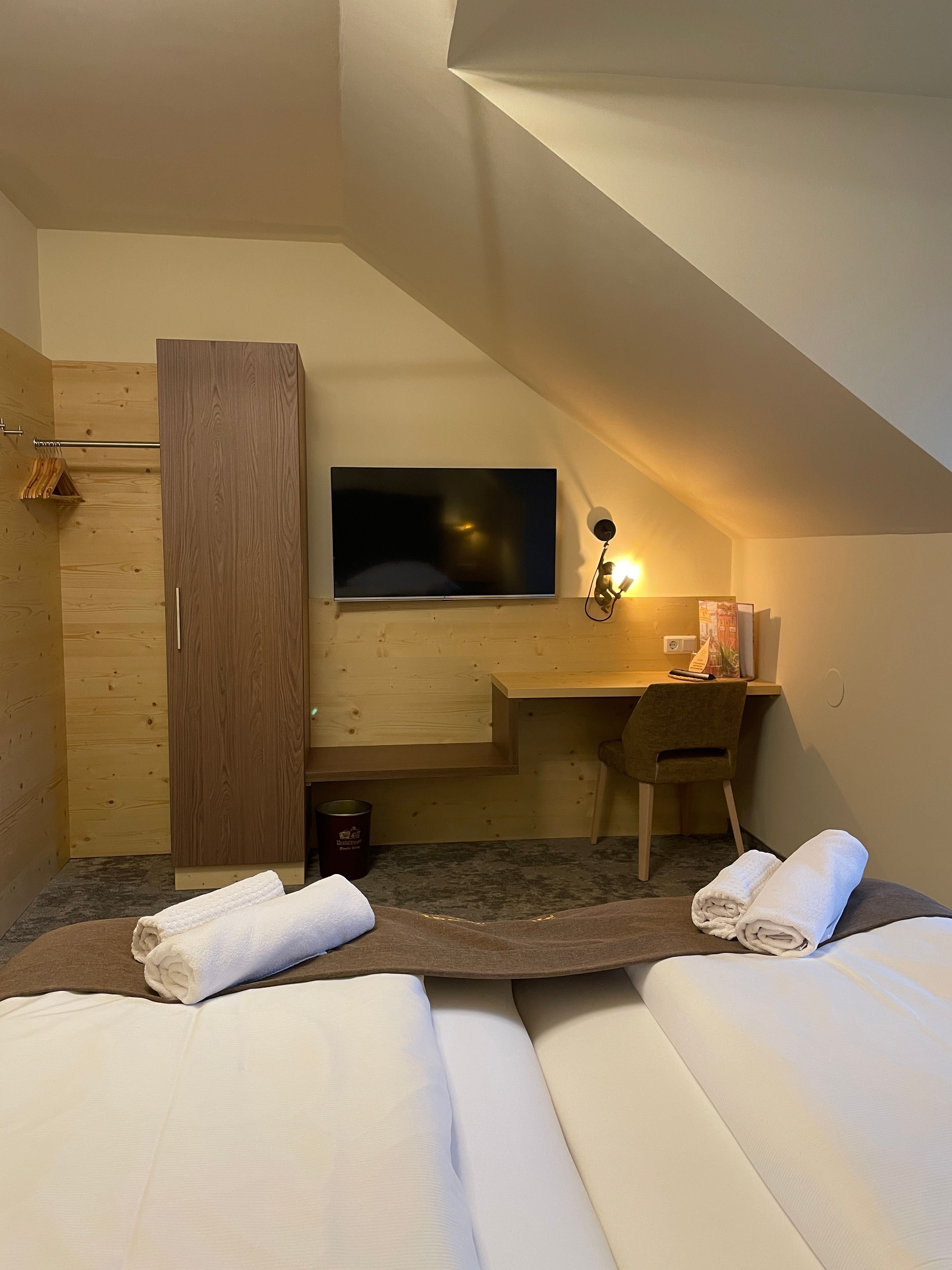 Gemütliches Doppelzimmer mit zwei Betten, einem Schreibtisch, einem Fernseher und einem Kleiderschrank.